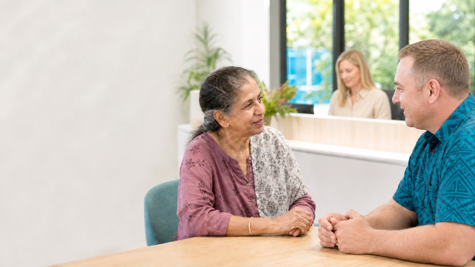 An older woman speaking with a client liaison at a bright office.